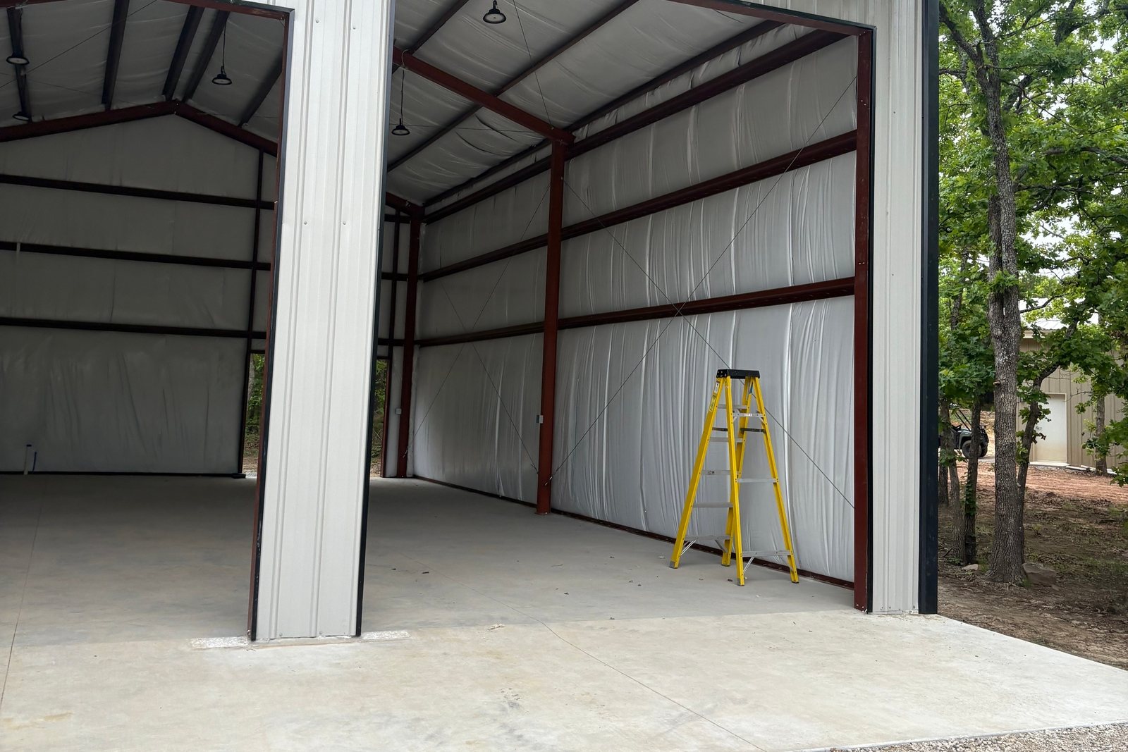 White metal building with an open bay and red steel framing inside
