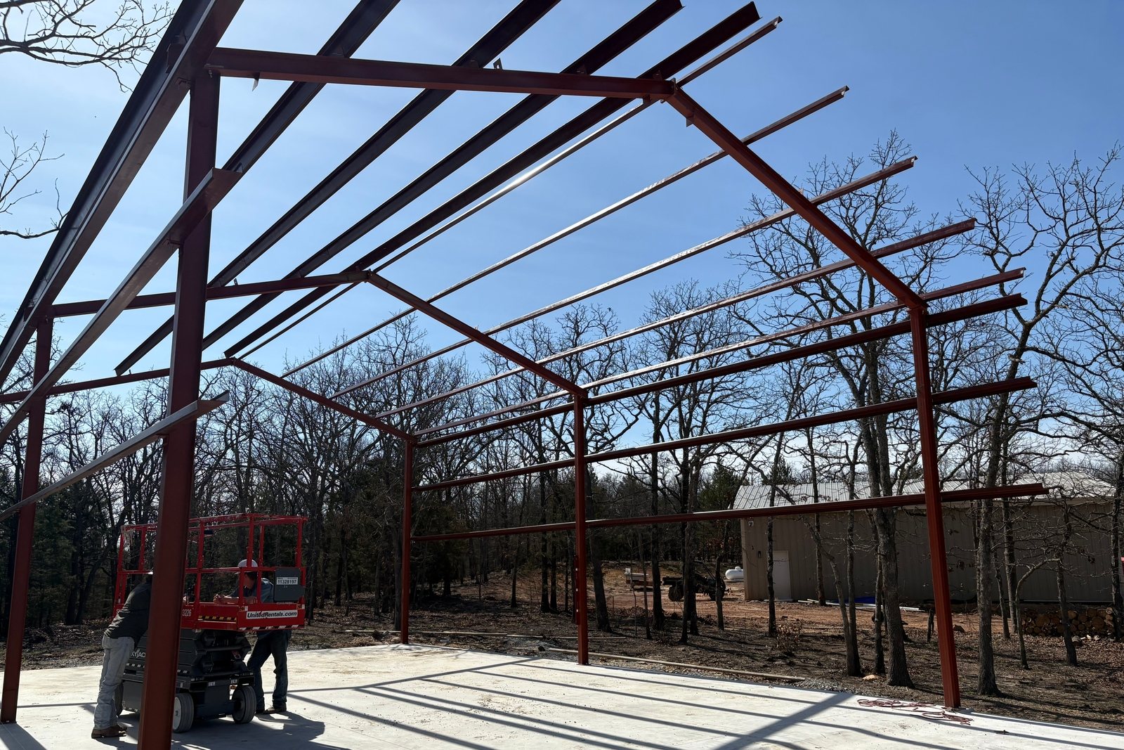 Red steel building frame standing on a concrete slab under a blue sky